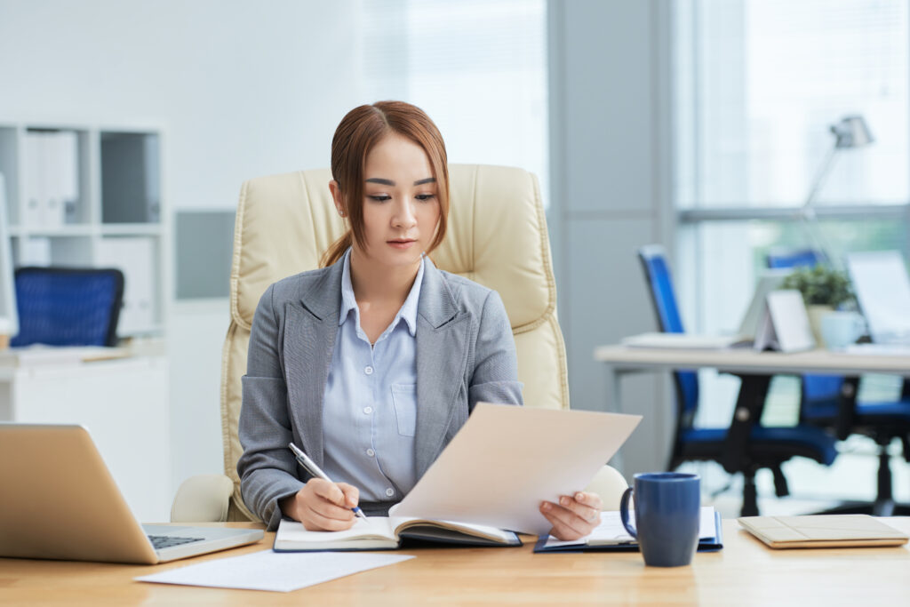 medium-shot-young-asian-woman-suit-sitting-desk-office-reading-document